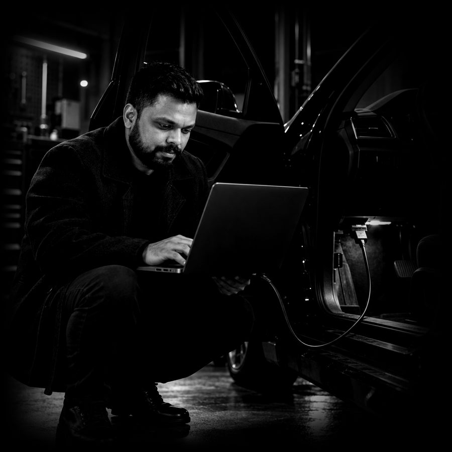 Adharna crouched by an open car door, laptop connected to the diagnostic port